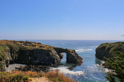 Scenic view of rocks in sea against clear blue sky