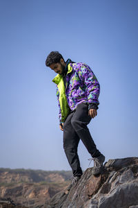 Young indian boy standing on the top of cliff wearing a snow jacket and track pants. 