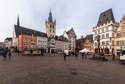 People on street by buildings in town against sky