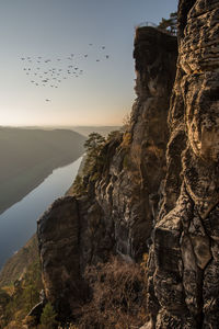 Birds flying over valley against clear sky during sunset