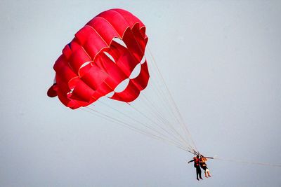 Low angle view of people paragliding against sky