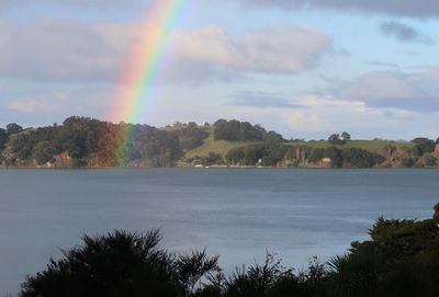 Scenic view of rainbow over lake against cloudy sky