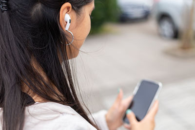 Crop young hispanic lady with smartphone listening to music in wireless earphones