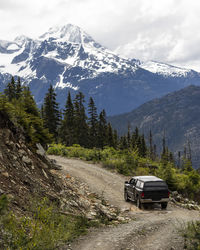 Modern vehicle driving along curvy logging road near rough slope during trip through snowy mountains in british columbia, canada