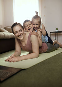 Cheerful boy and girl lying on mother exercising in living room