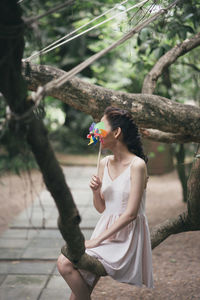 Woman holding colorful pinwheel toy while sitting on branch at park