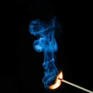 Close-up of burning matchstick against black background