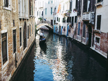 Man rowing gondola on canal amidst buildings