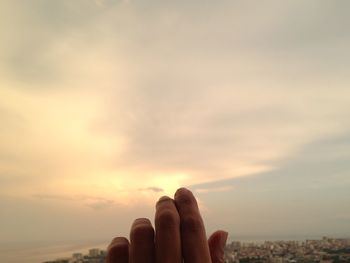 Close-up of hand against sea during sunset