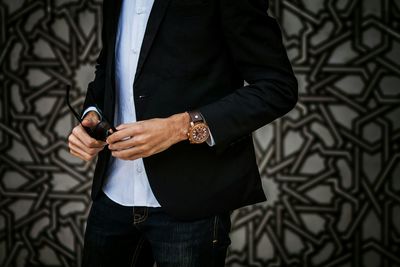 Midsection of fashionable man wearing suit while holding sunglasses