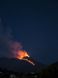 Panoramic view of the etna volcano illuminated by lava and the night sky.