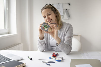 Smiling woman repairing electrical equipment at desk
