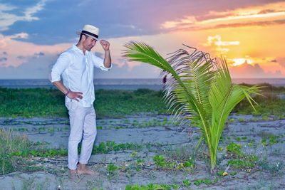 Side view of young man standing on land against sunset sky