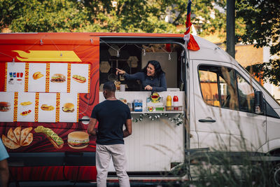 Happy saleswoman explaining menu to male customer while standing in food truck