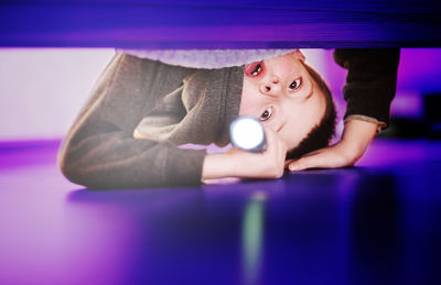 Scared little child boy looks under the bed with a flashlight on. fear of the dark