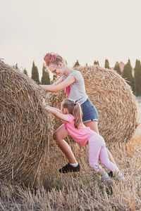 Full length of mother and daughter pushing hay bale on land