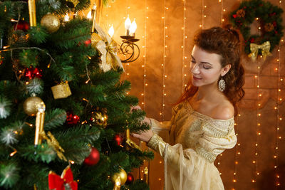 Cute woman in golden dress decorates christmas tree with christmas ball at