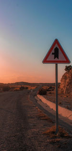 Road sign on field against clear sky during sunset