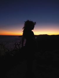 Silhouette woman standing on beach against sky during sunset