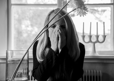 Portrait of woman with hands covering mouth sitting at home