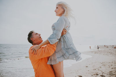 Side view of smiling man lifting woman at beach