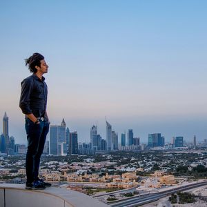 Full length of young man standing on building terrace looking over cityscape