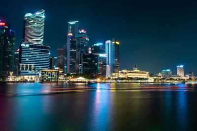 Illuminated city by river against sky at night