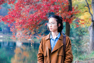 Thoughtful man standing at lakeshore during autumn