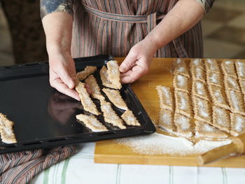 An elderly woman is hands place sliced raw biscuits on a baking sheet in the oven.