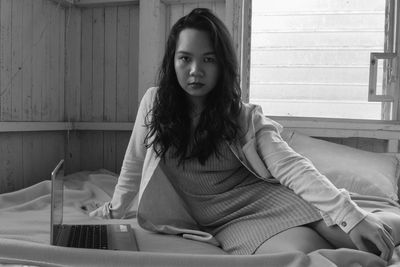 Portrait of young woman sitting with laptop on bed