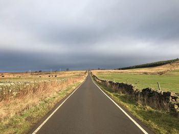 Empty road amidst field against sky