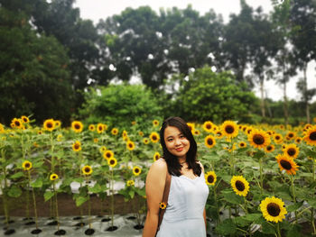 Portrait of young woman standing against yellow flowering plants