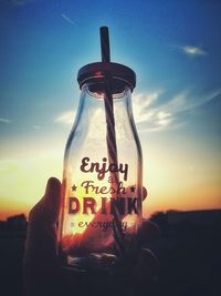 Close-up of hand holding bottle against sky during sunset