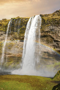 Idyllic rainbow at seljalandsfoss from mountain against cloudy sky during sunset