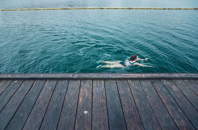 Woman swimming solo next to wooden dock in cold water in cdenmark