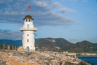 Turkey, alanya - november 9, 2020. white port lighthouse on background of mountains, sky and sea