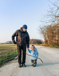 Grandfather and daughter walking on road against clear sky