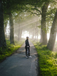 Rear view of women riding bicycle on road amidst trees in forest