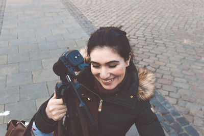 Smiling young woman holding tripod on street