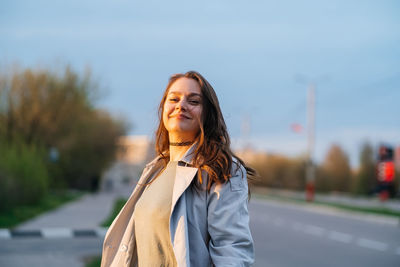 Beautiful smiling girl with long hair in a grey trench coat outdoors on the street spring