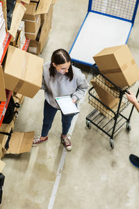 High angle view of woman using digital tablet while analyzing cardboard boxes in industry