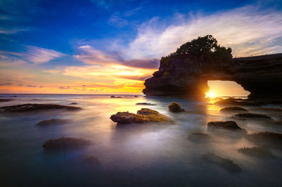 Scenic view of pura tanah lot in sea against sky during sunset