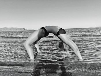 Side view of young woman wearing bikini while exercising in sea on shore at beach