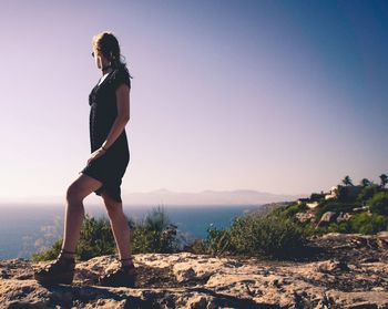 Side view of young woman standing against clear blue sky