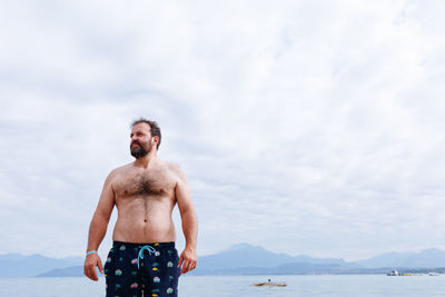Portrait of shirtless man standing against sea