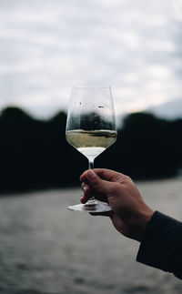 Cropped hand holding wineglass by sea