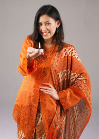 Portrait of smiling woman holding diya against gray background