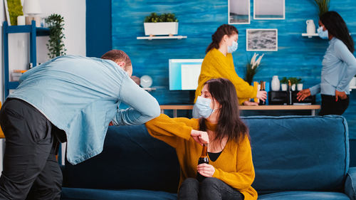 Cheerful couple wearing mask doing elbow bump at home