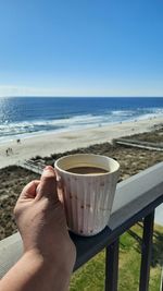 Midsection of man with drink at beach against sky