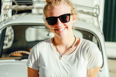 Portrait of young woman wearing sunglasses against car